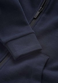 Marinblå zip-up sweatshirt med ribbade manschetter, med en slät textur, plattlåsta sömmar och en svart dragkedja med logodetalj.