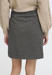 Sort-hvidternet nederdel i et tekstureret stof, med elastisk talje og lige snit, der når midt på låret.