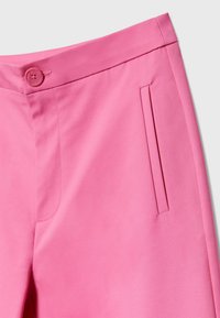 Pantalon rose avec une texture lisse, une taille boutonnée et des poches latérales. Présente des coutures nettes et une coupe ajustée.