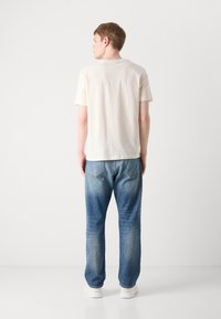 Light-colored short-sleeve t-shirt paired with medium-wash denim jeans, featuring a relaxed fit and subtle fading. Clean, casual look.