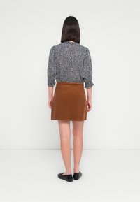Brown corduroy skirt with a straight shape, paired with a black-and-white patterned blouse. Black flat shoes complete the outfit.