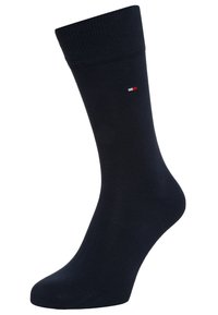 Chaussette en coton marine avec un haut côtelé, une texture lisse, et un petit détail logo rouge et blanc près du poignet. Longueur classique de type crew.