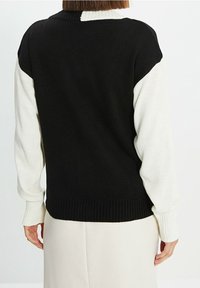 Czarnobiały sweter dziany z blokami kolorów. Posiada prążkowany kołnierz i mankiety. Tył wykonany bezszwowo z kontrastowymi rękawami.