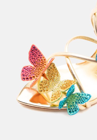 Χρυσό σανδάλι με ψηλό τακούνι και τρεις διακοσμητικές πεταλούδες σε ροζ, κίτρινο και μπλε στη λουρίδα των δαχτύλων, πάνω σε λευκό φόντο.