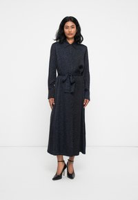 Rochie cambrată cu mâneci lungi, de culoare albastru închis, cu un model de imprimeu leopard, talie accentuată cu curea și țesătură fină. Pur și simplu cu pantofi cu toc înalt negri.