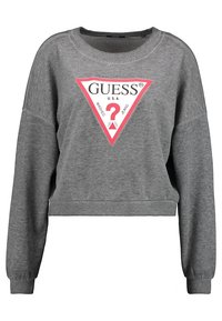 Harmaa lyhythihainen collegepaita, joka on valmistettu puuvillasekoitteesta. Tässä paidassa on suuri punavalkoinen kolmio-logo, jossa on sana "GUESS" ja kysymysmerkkiyksityiskohta.