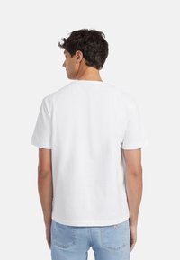 Camiseta de algodón blanca de manga corta, cuello redondo y corte recto. La vista trasera muestra una textura suave y un diseño simple.