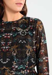 Abito nero floreale con maniche lunghe, caratterizzato da motivi intricati in oro, rosso e verde, realizzato in tessuto leggero e trasparente.