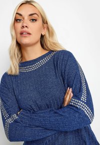 Blauer Strickpullover mit geripptem Muster, rundem Ausschnitt und metallischen Nietenakzenten an den Schultern und Ärmeln.