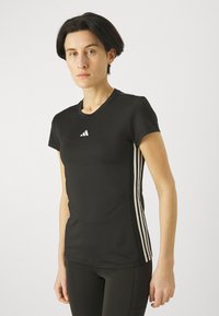 Musta lyhythihainen urheilupaita pyöreällä kaula-aukolla ja kolme valkoista vaakaraitaa sivuilla. Rinnassa on Adidas-logo.