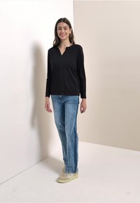 Black long-sleeve top with a V-neck, paired with light blue straight-leg jeans and beige sneakers. Minimalist design and casual fit.