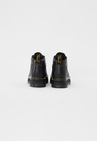 Botas de cuero negro con costuras amarillas y etiqueta 'With Bounce', con punta redondeada y suelas de goma duraderas, vistas desde atrás.