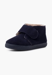 Botas de tobillo de ante azul marino con una correa de Velcro, forro beige y suela de goma negra texturizada. Diseñadas para la comodidad y la facilidad de uso.