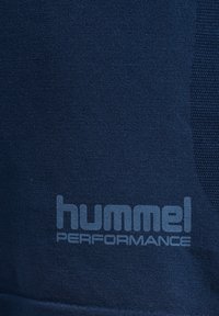 Granatowy materiał o gładkiej fakturze z wyraźnym, jasnoniebieskim logo "hummel PERFORMANCE" nadrukowanym na nim.