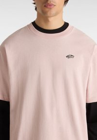 Ljusrosa bomulls T-shirt med svart krage, som har en liten svart Vans-logga på bröstet och korta ärmar.