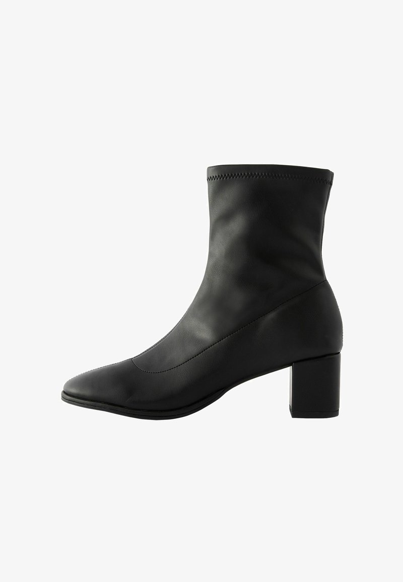 Svart ankelboot i slät läder, med spetsig tå och klack i blockstil. Sömsdetaljer löper längs ovansidan för extra struktur.