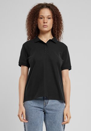 Svart polo skjorte laget av bomull, med klassisk krage, korte ermer og en subtil frontknapping. Kombinert med lyse denimjeans.