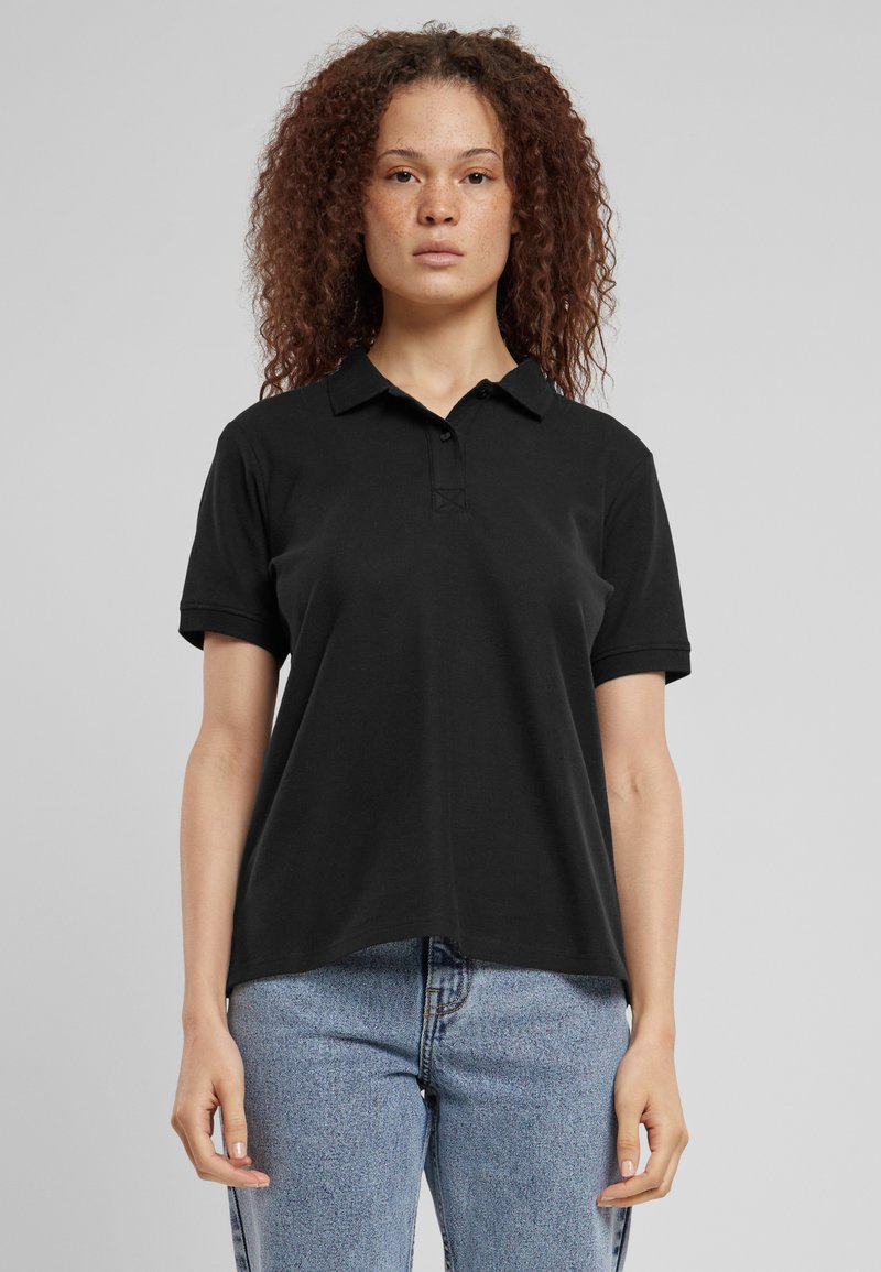 Svart polo skjorte laget av bomull, med klassisk krage, korte ermer og en subtil frontknapping. Kombinert med lyse denimjeans.