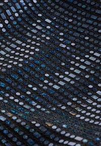 Tessuto nero con un motivo di piccole paillettes circolari e rettangolari lucide nelle tonalità di blu e argento, creando un aspetto testurizzato.