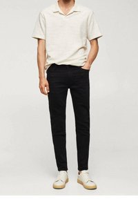 Polo shirt blanc texturé à manches courtes associé à un jean noir ajusté et des baskets crème. Tenue décontractée au design simple et aux couleurs contrastées.