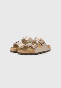 Sandalias metálicas doradas con dos correas ajustables, plantilla de corcho y suela de goma texturizada. El herraje cuenta con hebillas en bronce.