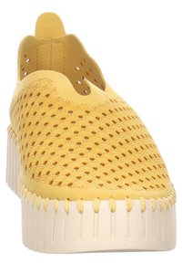 Scarpa gialla slip-on realizzata in materiale perforato con motivo curvo, dotata di una suola bianca spessa e dettagli testurizzati lungo il bordo.