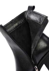 Zwarte leren enkelboot met een ritsluiting. Interieur heeft een zachte, donker suede-achtige voering; het exterieur heeft een gestructureerde afwerking.