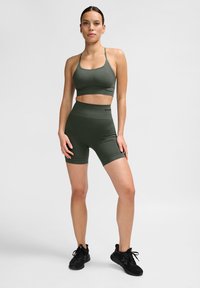 Donkergroene sportset bestaande uit een cropped sportbeha en hoge shorts. Gemaakt van rekbaar materiaal, met minimale branding en zonder patronen.