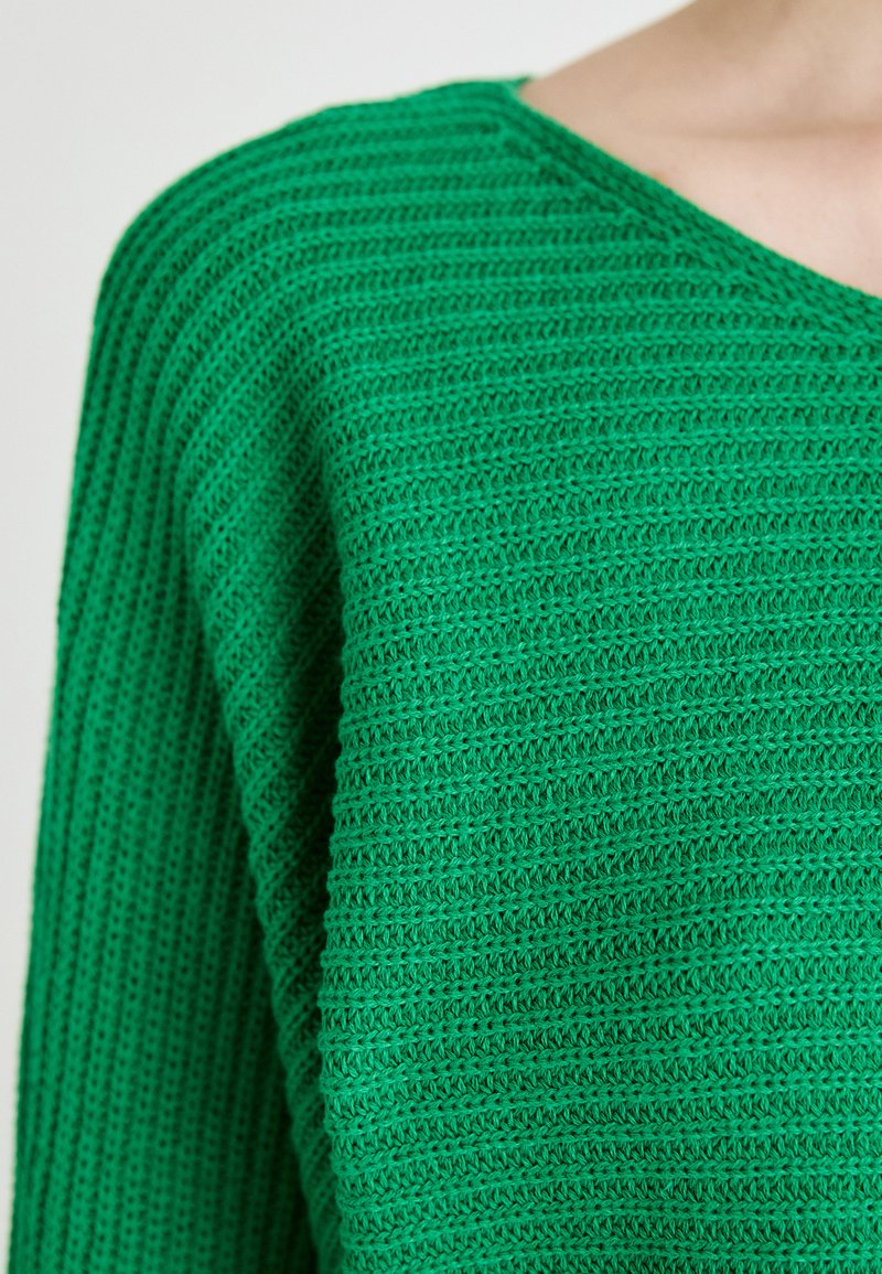 Grüner, gestrickter Pullover mit V-Ausschnitt, der ein strukturiertes Muster aus horizontalen Streifen aufweist. Hergestellt aus einem leichten, atmungsaktiven Material.