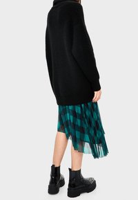 Maglione nero oversize a maglia con colletto alto, indossato sopra una gonna midi trasparente a righe blu e nere, abbinato a stivaletti neri con borchie.