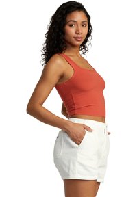 Rust-colored ribbed crop top and white corduroy shorts with side pockets. Straight fit and zipper closure on the shorts.