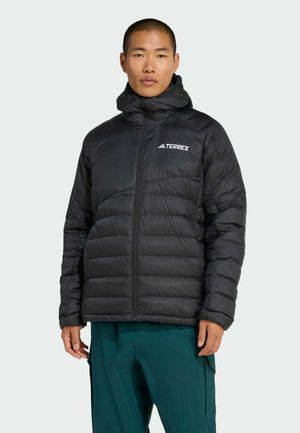 Svart puffjacka med hög krage, dragkedjestängning och texturerad, kviltad design. Har en vit logotyp på vänster bröst.