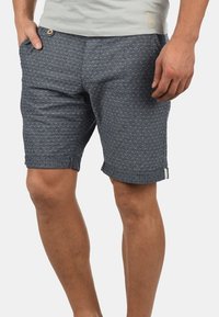 Shorts pour hommes bleu marine avec motifs clairs subtils, fabriqués en tissu texturé. Dotés de poches latérales et de revers roulés pour une coupe décontractée.