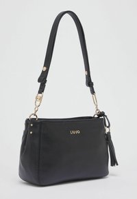 Sac à main en cuir noir avec une texture lisse, des accents en métal doré et une bandoulière amovible, agrémenté d'un détail pompon.