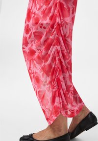 Prozorna roza tkanina z rdečim cvetličnim vzorcem, pregrnjena in nabrana čez spodnji del noge, kombinirana s črnimi balerinkami.