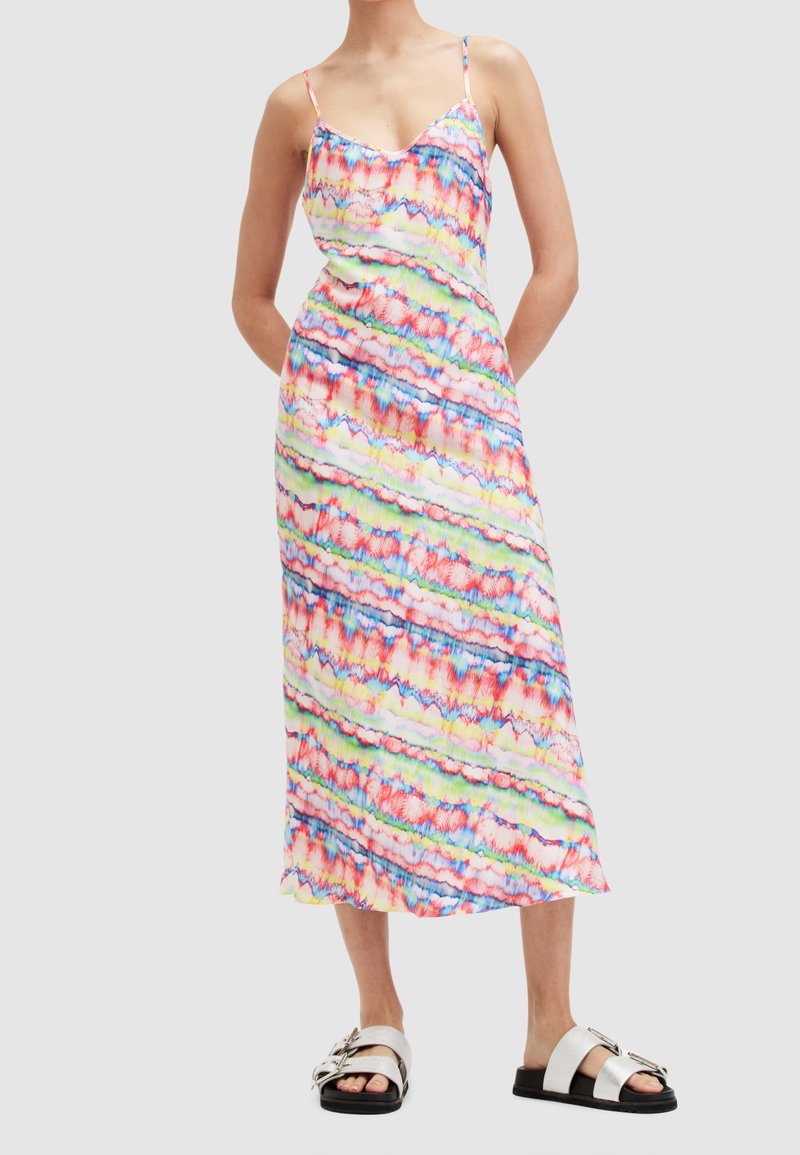 Mehrfarbiges Maxikleid mit dünnen Trägern, das ein wellenförmiges Muster in Rot, Blau, Grün und Weiß zeigt. Kombiniert mit schwarzen und silbernen Sandalen.