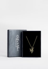 Guld fugleformet halskæde med en lille ædelsten, præsenteret i en sort fløjl-foret boks med en struktureret grå yderside.