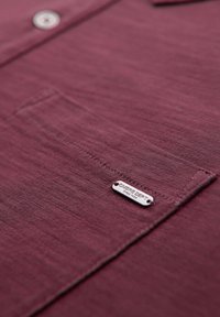 Polo shirt bordeaux a trama con chiusura a bottoni, taschino sul petto e tag argento "OMERE DEPT".