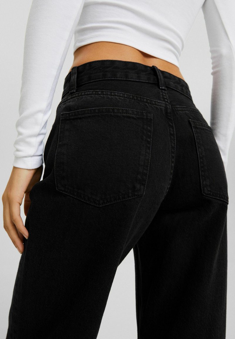 Jeans in denim nero a vita alta con design a gamba dritta, dotati di due tasche posteriori e una cintura visibile. Il tessuto ha una texture liscia.