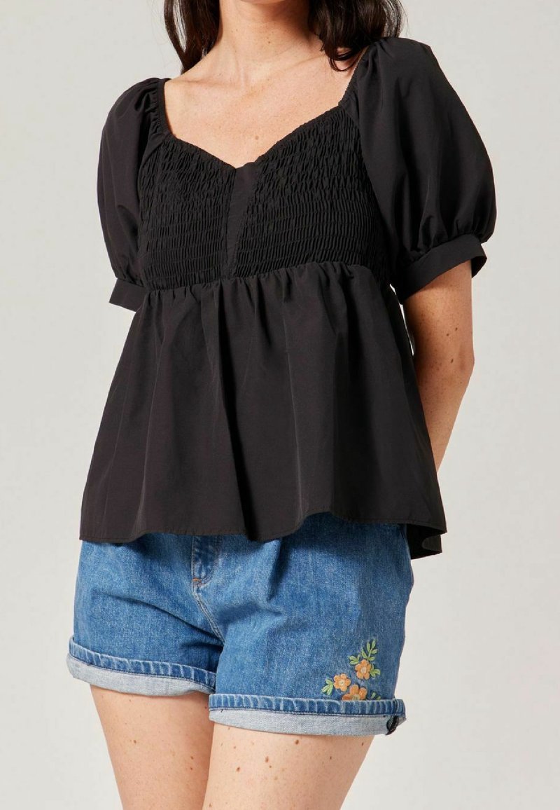 Black short-sleeve blouse with a smocked bodice and loose peplum design, paired with denim shorts featuring floral embroidery on hem.