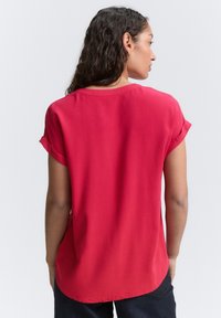 Rote kurzärmelige Bluse mit Rundhalsausschnitt und einem leicht abgerundeten Saum. Der Stoff hat eine glatte Textur, mit umgeschlagenen Ärmeln und einem lockeren Schnitt.