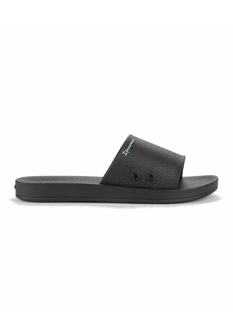 Sandalias de slide negras con un upper texturizado y dos agujeros decorativos; diseñadas con una suela plana y una silueta simple. Logo de la marca visible.