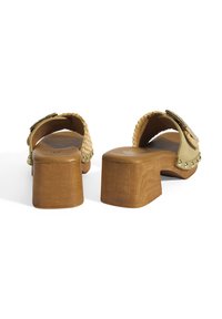 Houten klompen met een tan leren band, voorzien van geweven details en decoratieve studs langs de rand, met een vierkante hakdesign.
