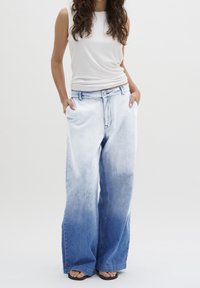 Jean en denim à jambes larges avec un design dégradé, passant du bleu clair en haut au bleu foncé en bas, présentant un style classique à cinq poches.