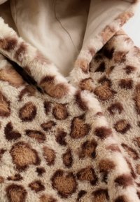 Material din blană artificială cu imprimeu de leopard, având o bază crem, cu o textură moale și nuanțe variate de pete maro, creat pentru o îmbrăcăminte confortabilă.