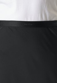 Ceinture noire Calvin Klein avec logo en relief, texture lisse, coupe basse et tissu doux et extensible pour le confort.