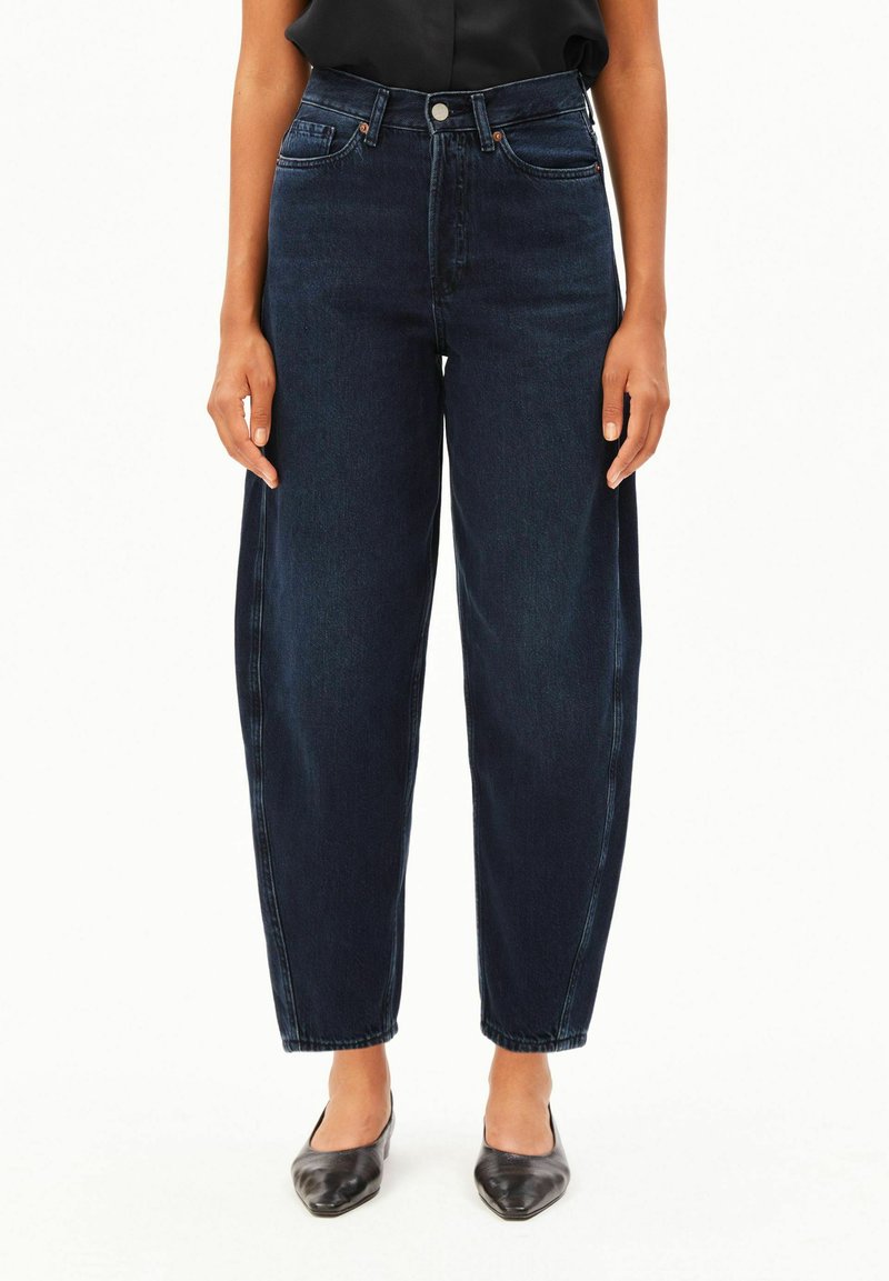 Person wearing dark blue high-waist wide-leg jeans paired with black pointed-toe shoes and a tucked-in black top.