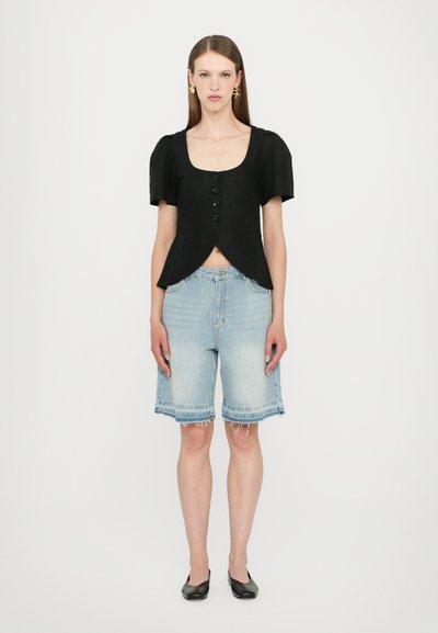 Svart cropped topp med rund hals og pufferm, med tre knapper. Lys bl�å denim Bermuda-shorts med usynlig søm, svarte flate sko.