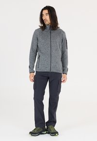 Grå fleece zip-up jakke med høj krave, parret med mørke cargo bukser og vandresko med grønne detaljer.