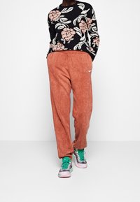Suéter negro con estampado floral rosa, combinado con pantalones de chándal coral holgados que presentan el logotipo blanco de Nike. Zapatillas con un patrón verde y rosa.